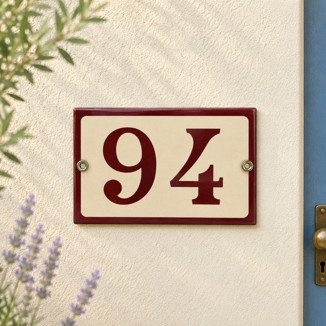 House number '94' plaque on a textured wall with plants and a door frame.