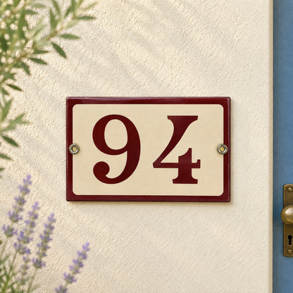 House number '94' plaque on a textured wall with plants and a door frame.