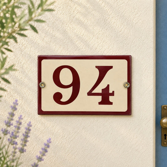 House number '94' plaque on a textured wall with plants and a door frame.