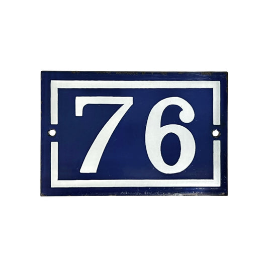 A rectangular French-style house number plaque with the number 76 in white on a dark navy blue background, bordered by a white frame with mounting holes.