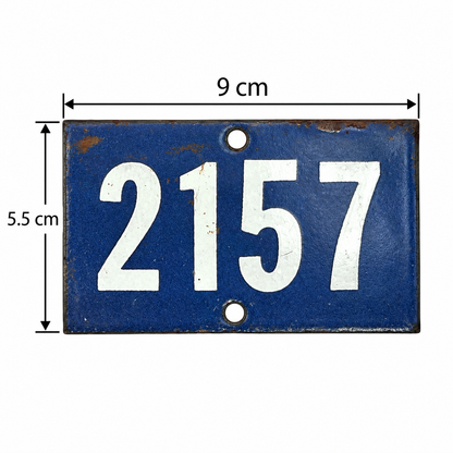 A rectangular blue vintage-style house number plaque with white numerals '2157' and measurement arrows showing 9 cm width and 5.5 cm height on a white background.