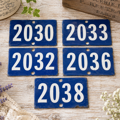 Collection of vintage French blue vitreous enamel number plaques displayed on a rustic wooden tabletop with lavender, a weathered wooden crate and trailing greenery. Authentic 1960s railway-style number signs arranged in a French country brocante setting.