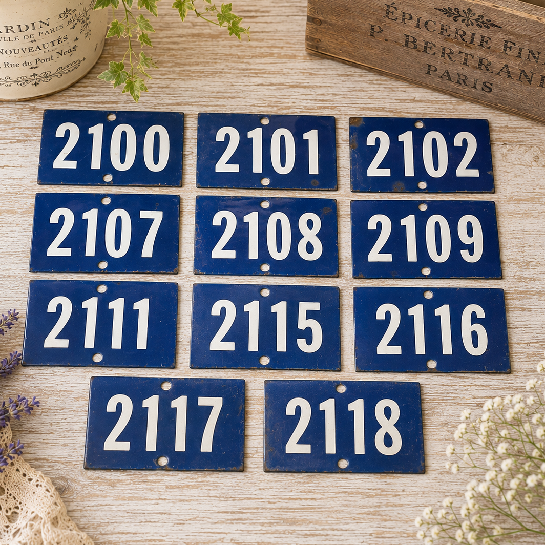 Collection of vintage French blue vitreous enamel number plaques displayed on a rustic wooden tabletop with lavender, a weathered wooden crate and trailing greenery. Authentic 1960s railway-style number signs arranged in a French country brocante setting.