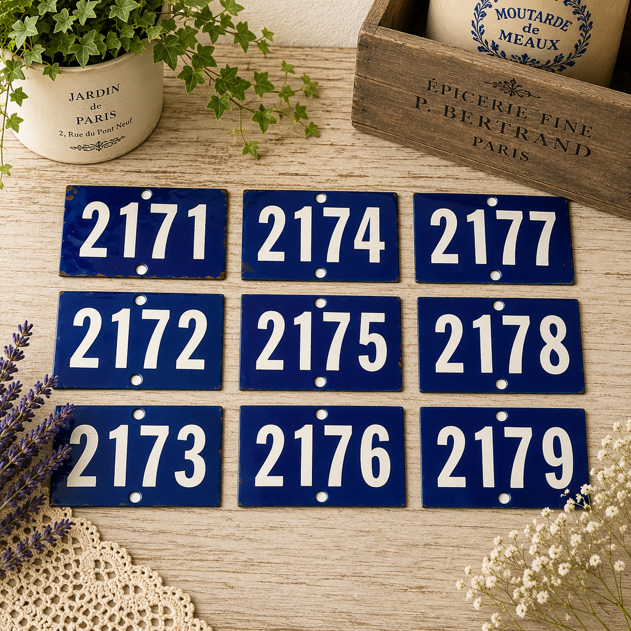 Collection of vintage French blue vitreous enamel number plaques displayed on a rustic wooden tabletop with lavender, a weathered wooden crate and trailing greenery. Authentic 1960s railway-style number signs arranged in a French country brocante setting.