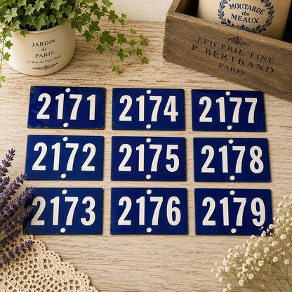 Collection of vintage French blue vitreous enamel number plaques displayed on a rustic wooden tabletop with lavender, a weathered wooden crate and trailing greenery. Authentic 1960s railway-style number signs arranged in a French country brocante setting.