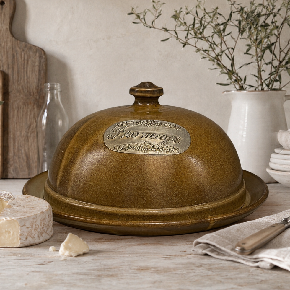 Ceramic covered dish on a wooden table with cheese and kitchen items in the background