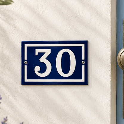 French vintage enamel blue and white door number 30 on a white stone wall with a door and a plant in the background, ideal for a French style home or rustic front door