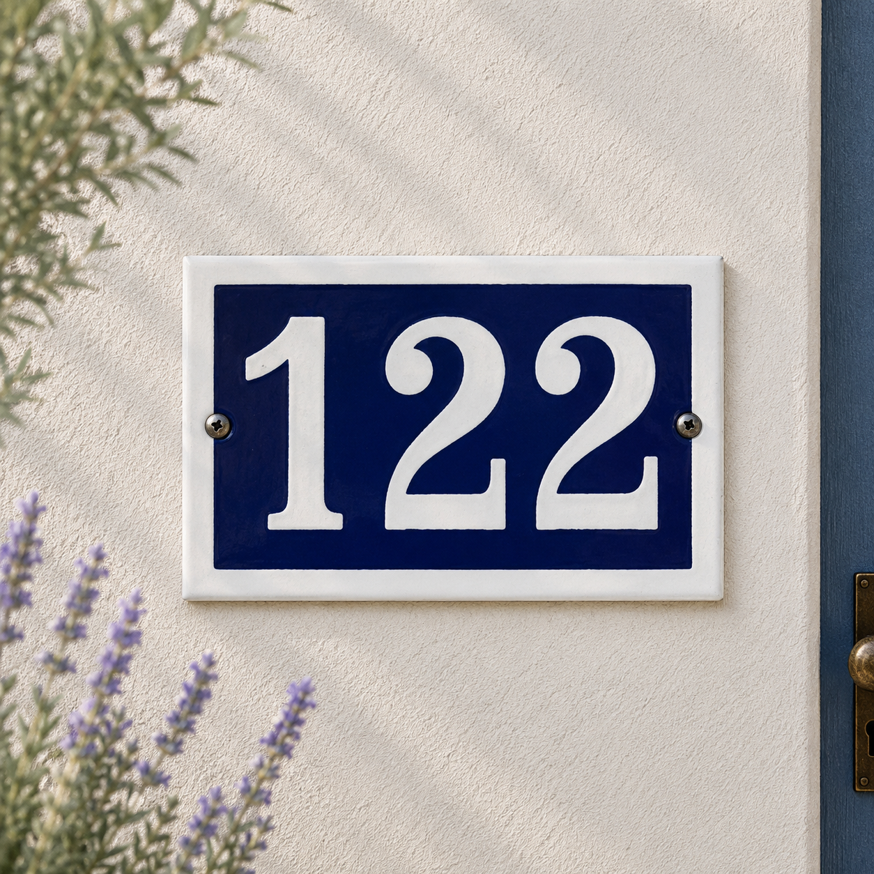 House number '122' on a blue and white sign mounted on a wall with plants and a door in the background.
