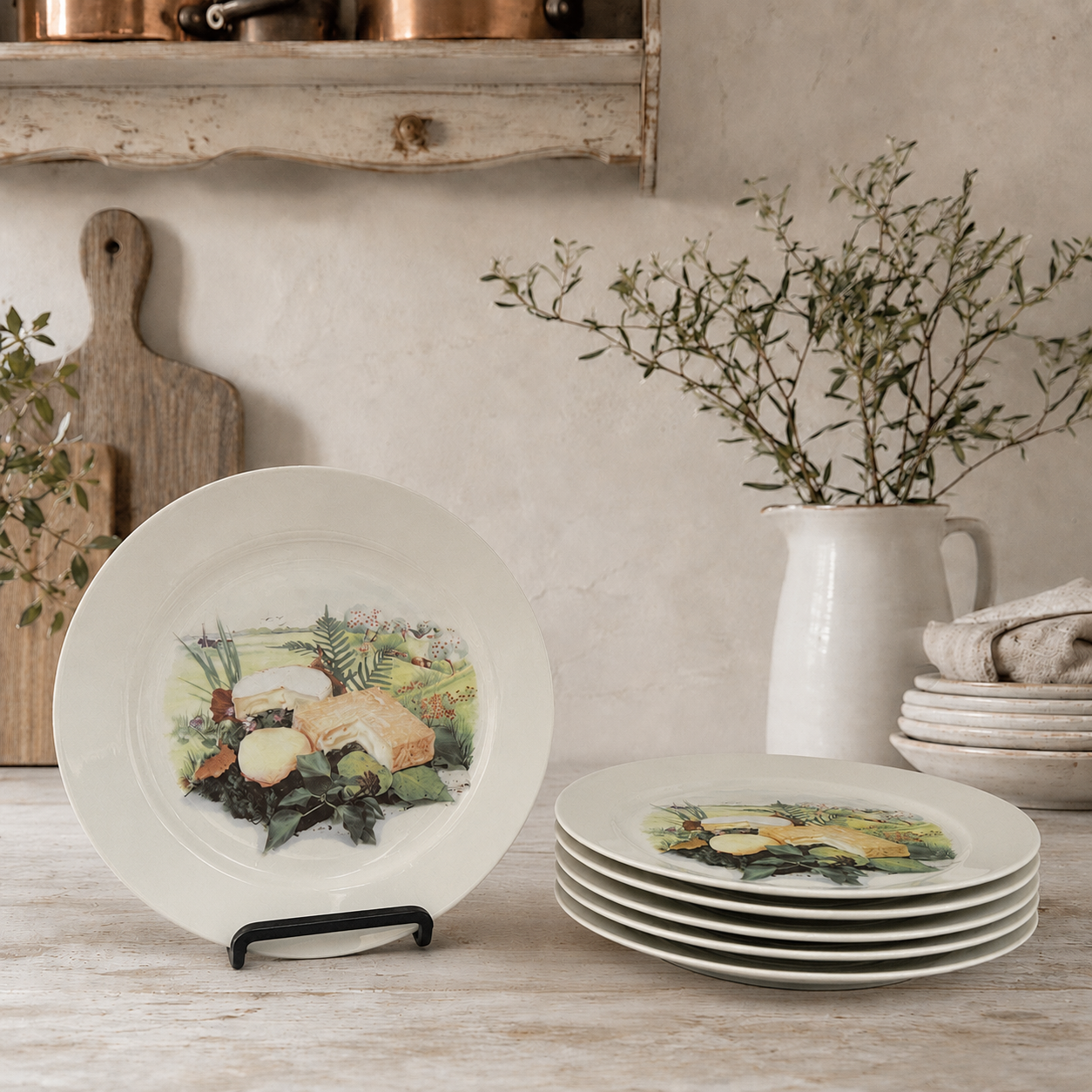 Set of French vintage cheese plates with a pattern detailing a selection of cheeses, one plate is on a display stand and the remaining 5 plates are stacked by the side. These are displayed on a countertop in a pale rustic kitchen background. Ideal for a cheese and wine evening or a farmhouse kitchen