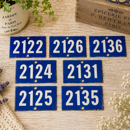 Collection of vintage French blue vitreous enamel number plaques displayed on a rustic wooden tabletop with lavender, a weathered wooden crate and trailing greenery. Authentic 1960s railway-style number signs arranged in a French country brocante setting.