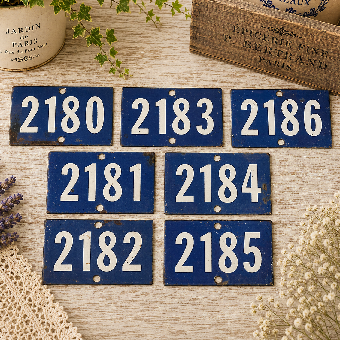 Collection of vintage French blue vitreous enamel number plaques displayed on a rustic wooden tabletop with lavender, a weathered wooden crate and trailing greenery. Authentic 1960s railway-style number signs arranged in a French country brocante setting.