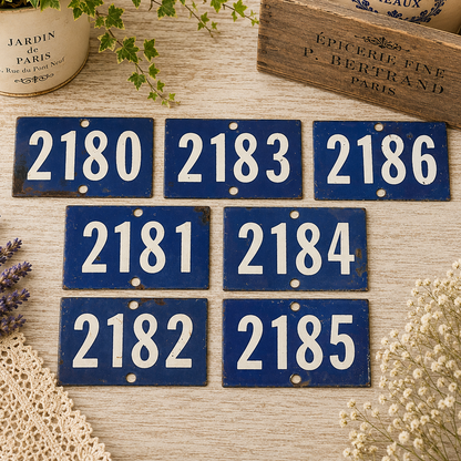 Collection of vintage French blue vitreous enamel number plaques displayed on a rustic wooden tabletop with lavender, a weathered wooden crate and trailing greenery. Authentic 1960s railway-style number signs arranged in a French country brocante setting.