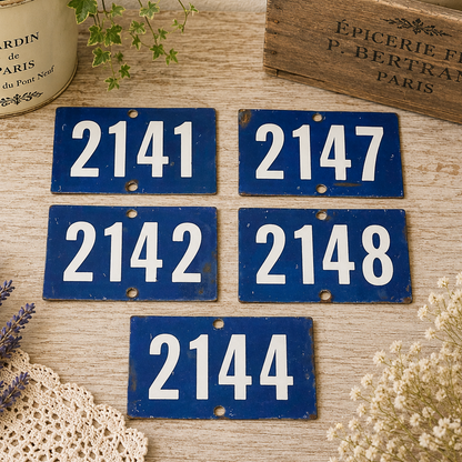Collection of vintage French blue vitreous enamel number plaques displayed on a rustic wooden tabletop with lavender, a weathered wooden crate and trailing greenery. Authentic 1960s railway-style number signs arranged in a French country brocante setting.