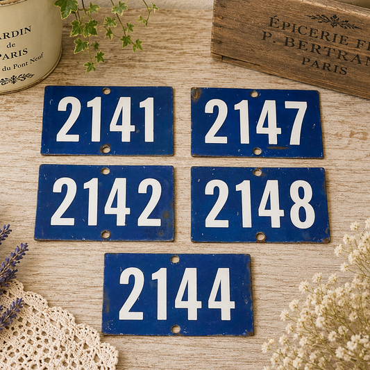 Collection of vintage French blue vitreous enamel number plaques displayed on a rustic wooden tabletop with lavender, a weathered wooden crate and trailing greenery. Authentic 1960s railway-style number signs arranged in a French country brocante setting.