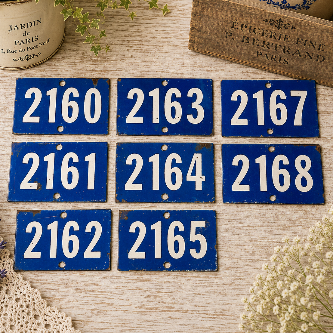 Collection of vintage French blue vitreous enamel number plaques displayed on a rustic wooden tabletop with lavender, a weathered wooden crate and trailing greenery. Authentic 1960s railway-style number signs arranged in a French country brocante setting.