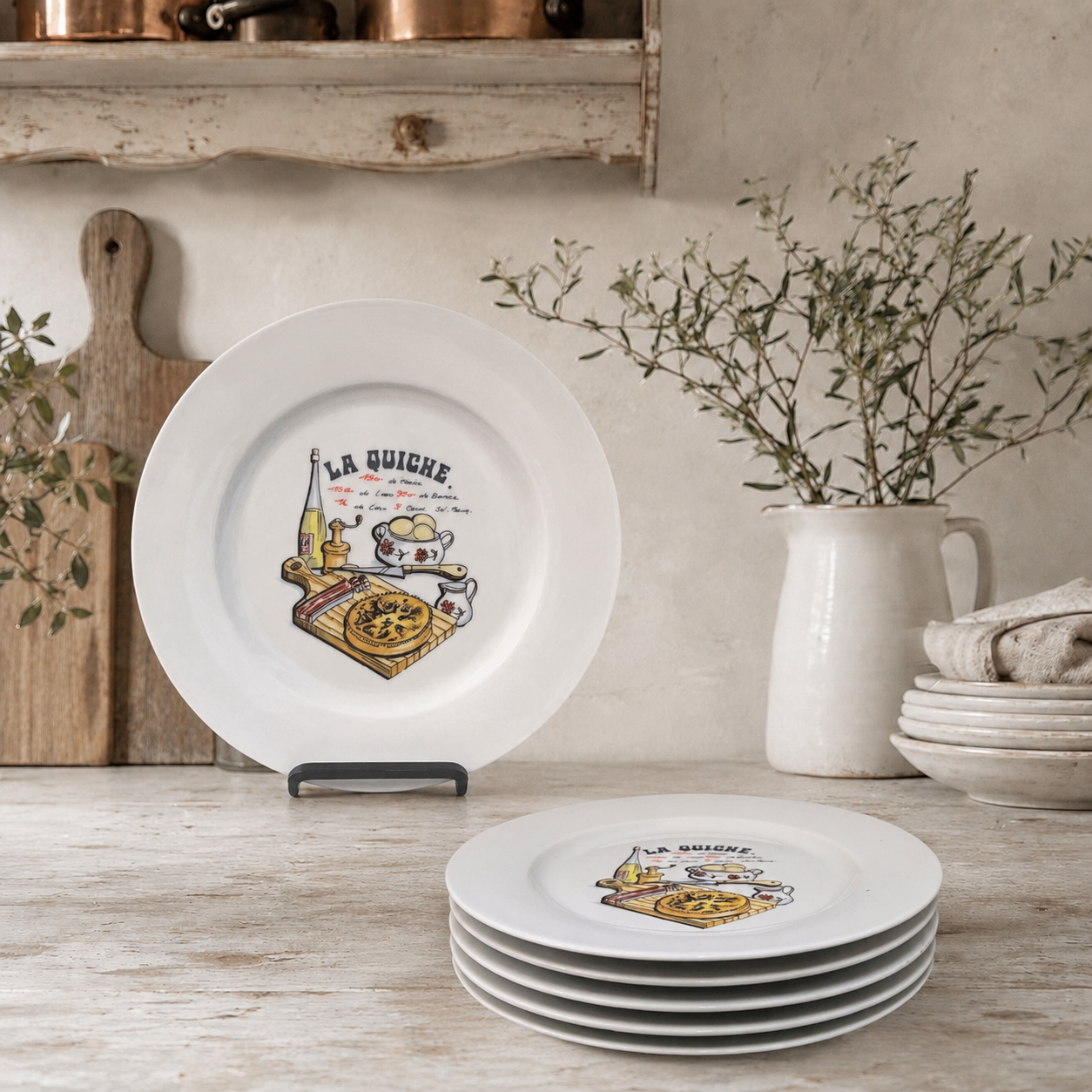 Set of white plates with decorative designs on a wooden surface, with a vase and branches in the background.