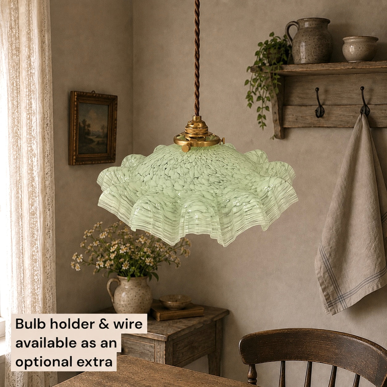 A light green ruffled glass pendant light hangs over a wooden dining table in a rustic room with a textured beige wall, a wooden shelf, and a hanging towel. A text overlay in the bottom left corner reads 'Bulb holder & wire available as an optional extra'.
