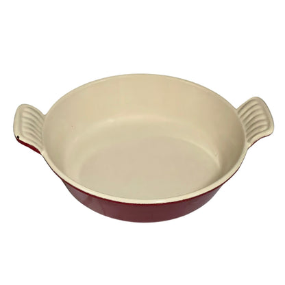 A round ceramic baking dish with a cream-colored interior and a dark red exterior, featuring two ribbed side handles.