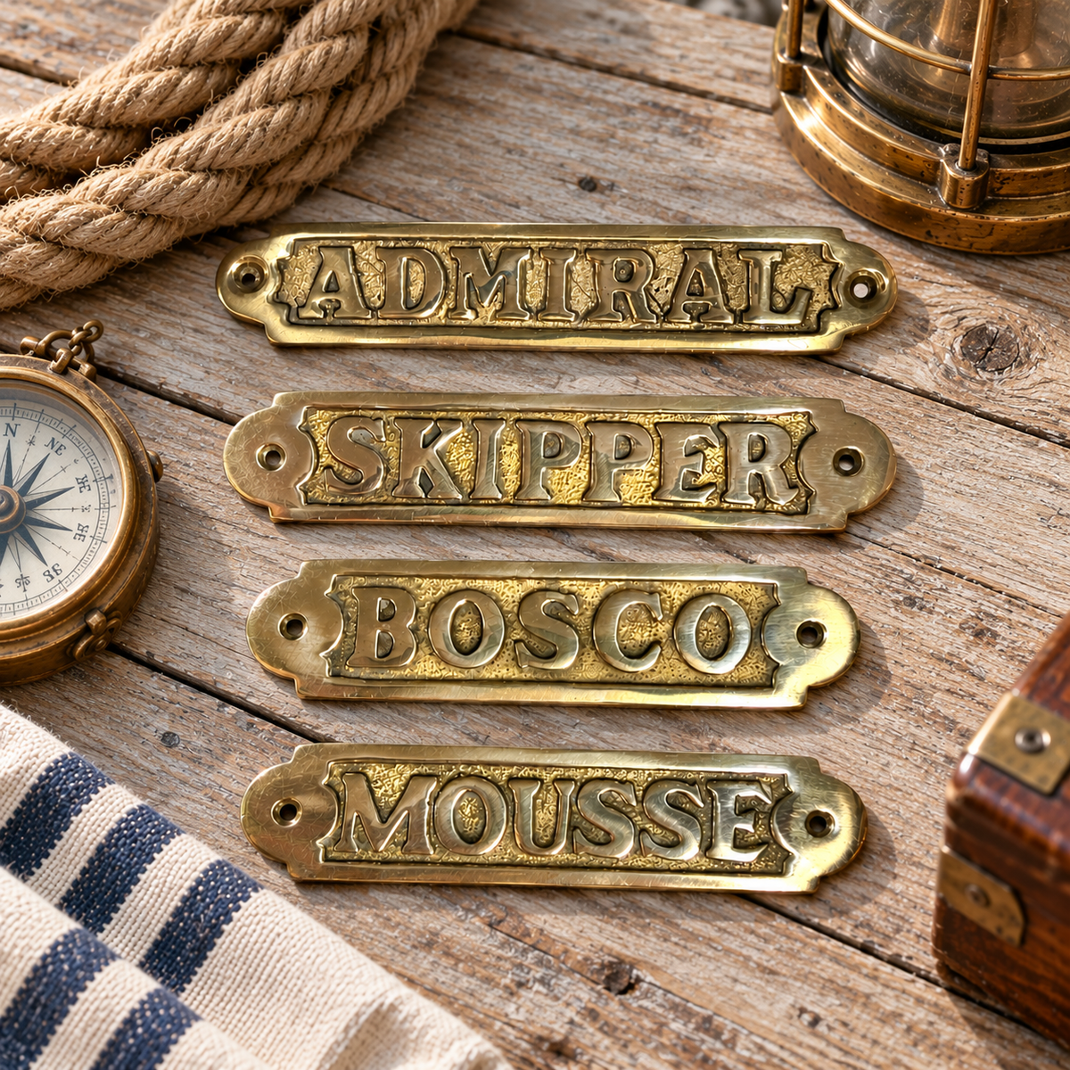 Set of four vintage French solid cast brass nautical door plaques displayed on pale weathered timber with maritime props including coiled rope, a vintage compass, brass lantern and striped fabric. The plaques read Admiral, Skipper, Bosco and Mousse and feature raised lettering, textured recessed backgrounds and fixing holes at each end. Authentic French brocante boat and yacht signs with traditional maritime terminology, suitable for cabin doors, nautical interiors, coastal decor and maritime collections.