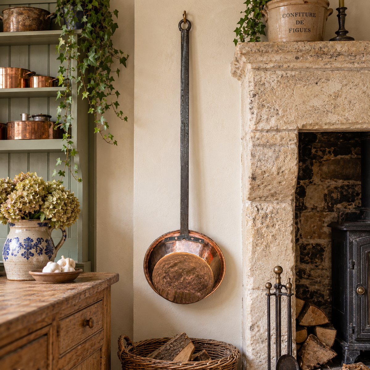 Antique French Villedieu Delalande copper pan with extra-long handle displayed beside a rustic stone fireplace in a French farmhouse kitchen.