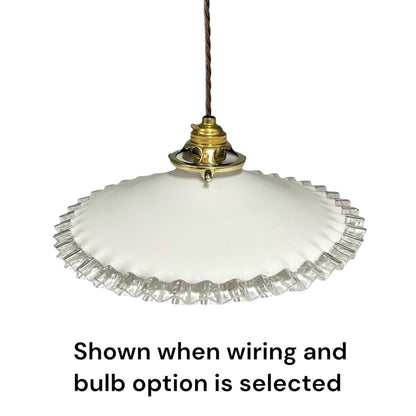 A white glass pendant light with a fluted clear glass rim and a brass-colored metal fixture, suspended by a dark cord. Text below reads 'Shown when wiring and bulb option is selected'.