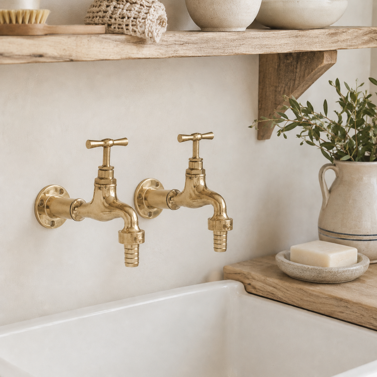 Gold faucet taps on a white sink with a wooden shelf and plant in the background