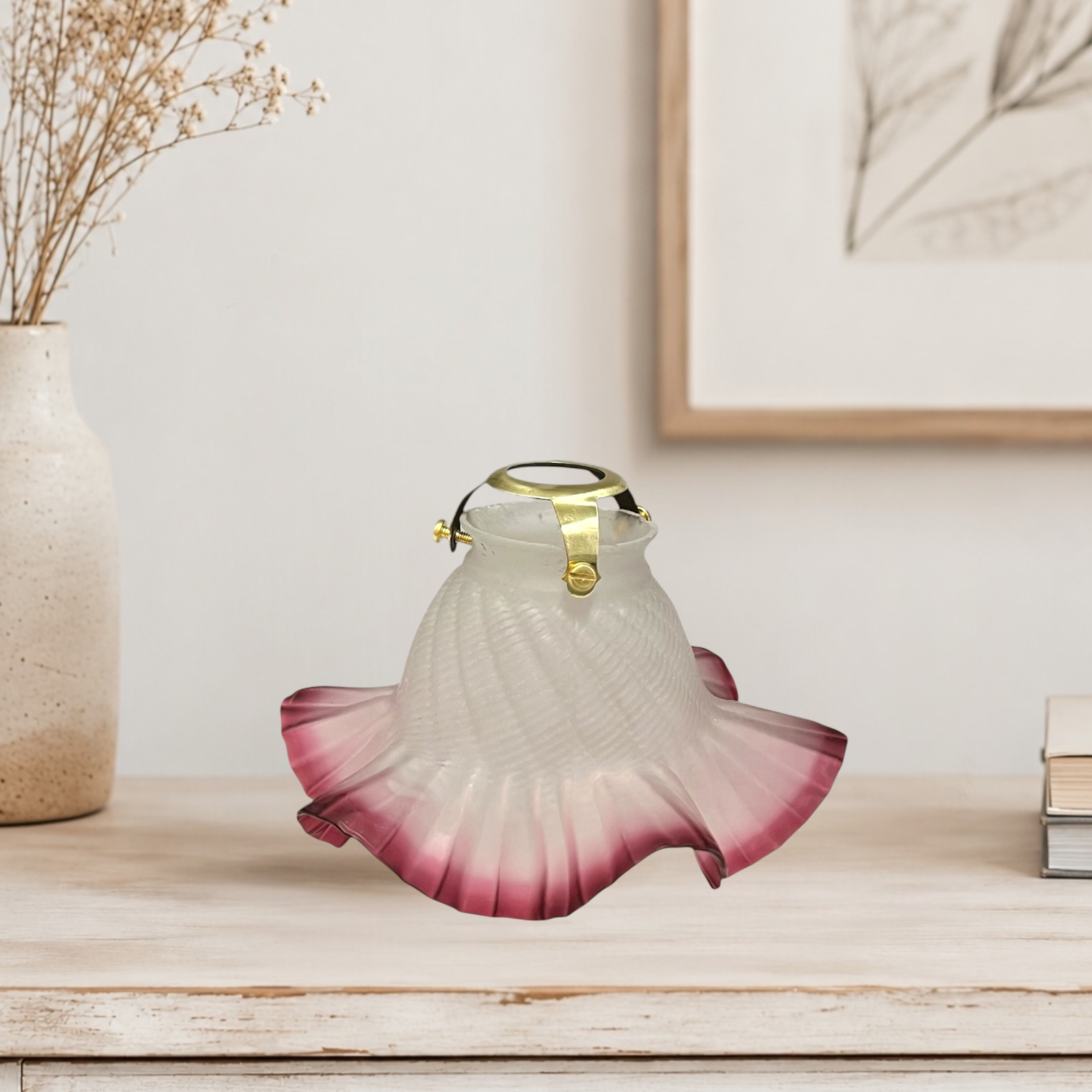 Decorative glass lamp with pink and white design on a wooden surface, with a vase and books in the background.