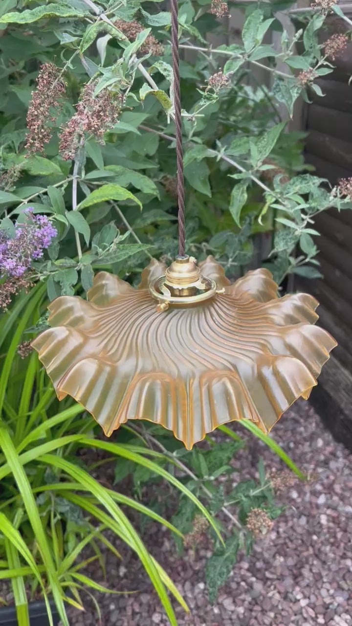 video of amber coloured vintage French  pendant light with a scalloped design in a garden