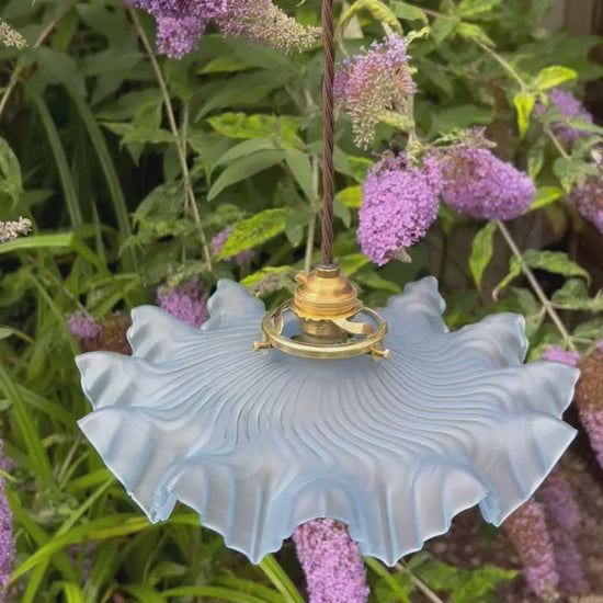 video showing a vintage blue glass lampshade with brass fittings and a brown twisted wire, hanging in a garden