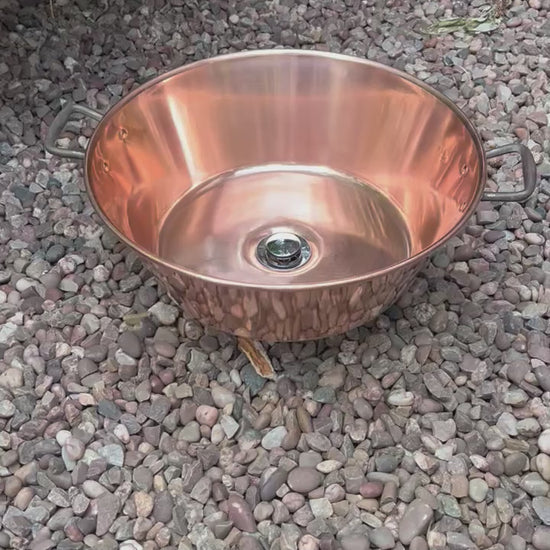 Video of French copper bowl upcycled into a copper sink with cast iron handles on gravel surface with plants in the background