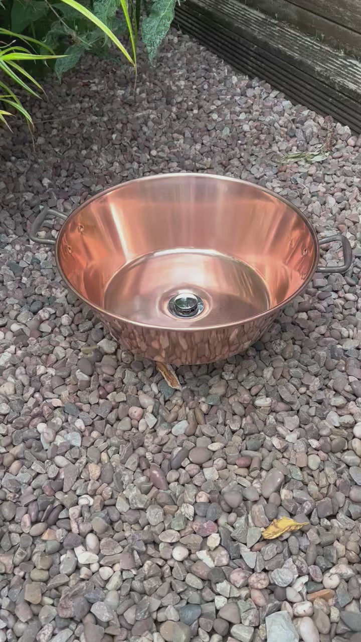 Video of French copper bowl upcycled into a copper sink with cast iron handles on gravel surface with plants in the background
