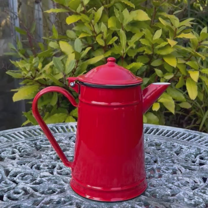 video of red enamel coffee pot on a table in a agrden 