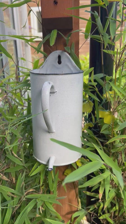 Video of French vintage enamel jug with a flat back and a spout in white and blue set in a garden