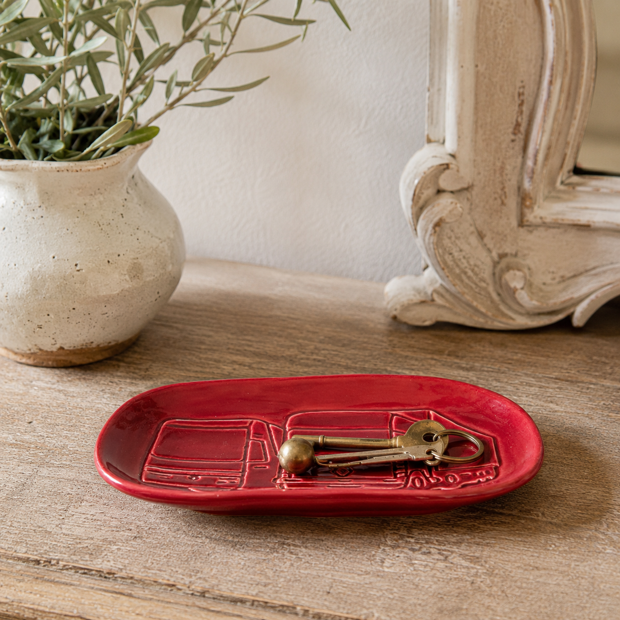 Vintage Renault ceramic trinket tray in deep red glaze with embossed Renault truck design, styled on a rustic wooden hallway table holding keys, beside a French country mirror and ceramic vase with greenery. Ideal as a key dish, catchall tray or automobilia display piece.