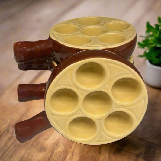 Set of 4 French brown and cream ceramic escargots dishes or plates each with 6 holes, stacked on a wooden table with a blurred image of a herb plant in the background
