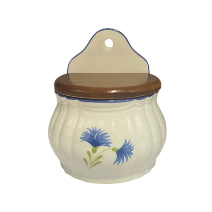 A ceramic jar with a ribbed cream-colored body, a dark brown wooden lid, and a matching hanging tab on top. The jar is decorated with a blue and green cornflower design on the front.