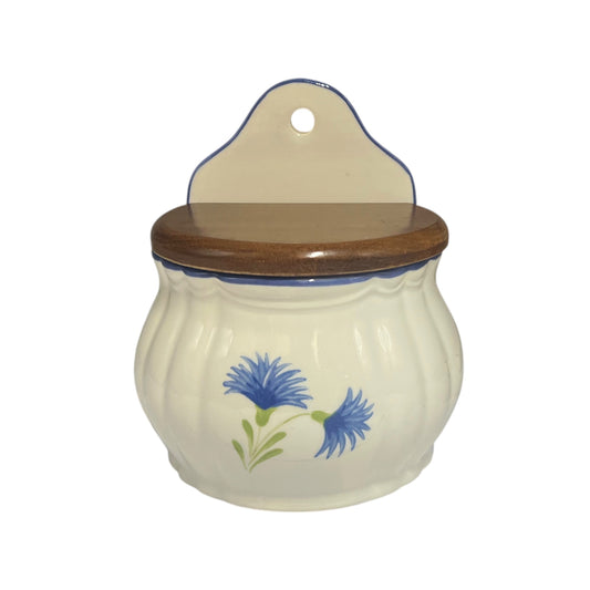 A ceramic jar with a ribbed cream-colored body, a dark brown wooden lid, and a matching hanging tab on top. The jar is decorated with a blue and green cornflower design on the front.