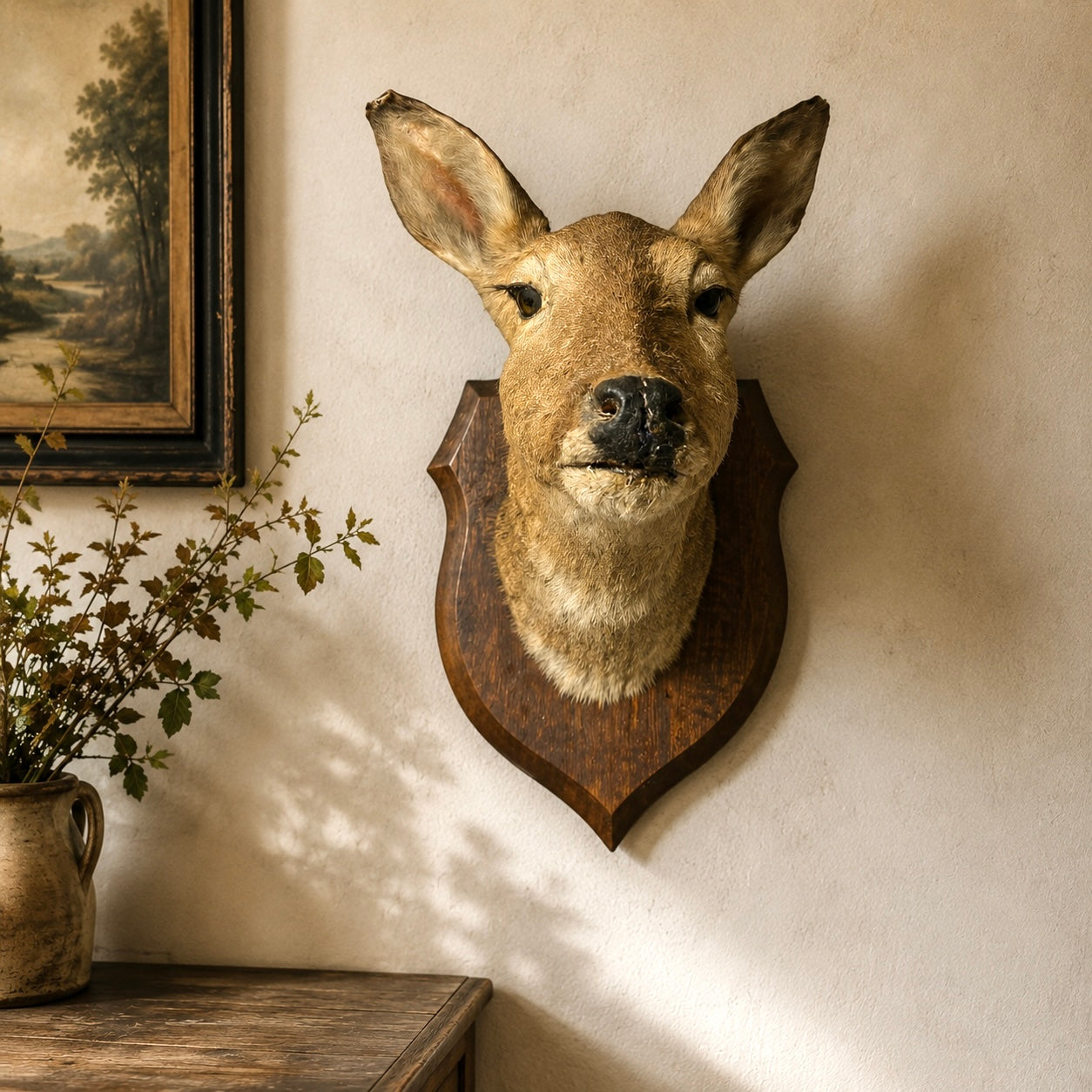 Trophied deer head mounted on a wall with a painting and plant in the background