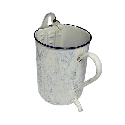 A vintage enamel pitcher with a white marbled finish, a dark blue rim, a metal pouring spout, and a carrying loop on a white background.