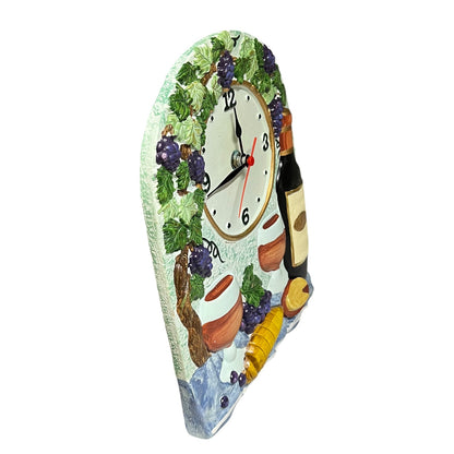 A decorative wall clock shaped like a wine bottle label, featuring a painted grapevine with purple grapes, a white clock face, wine bottles, and small terracotta pots on a plain white background.