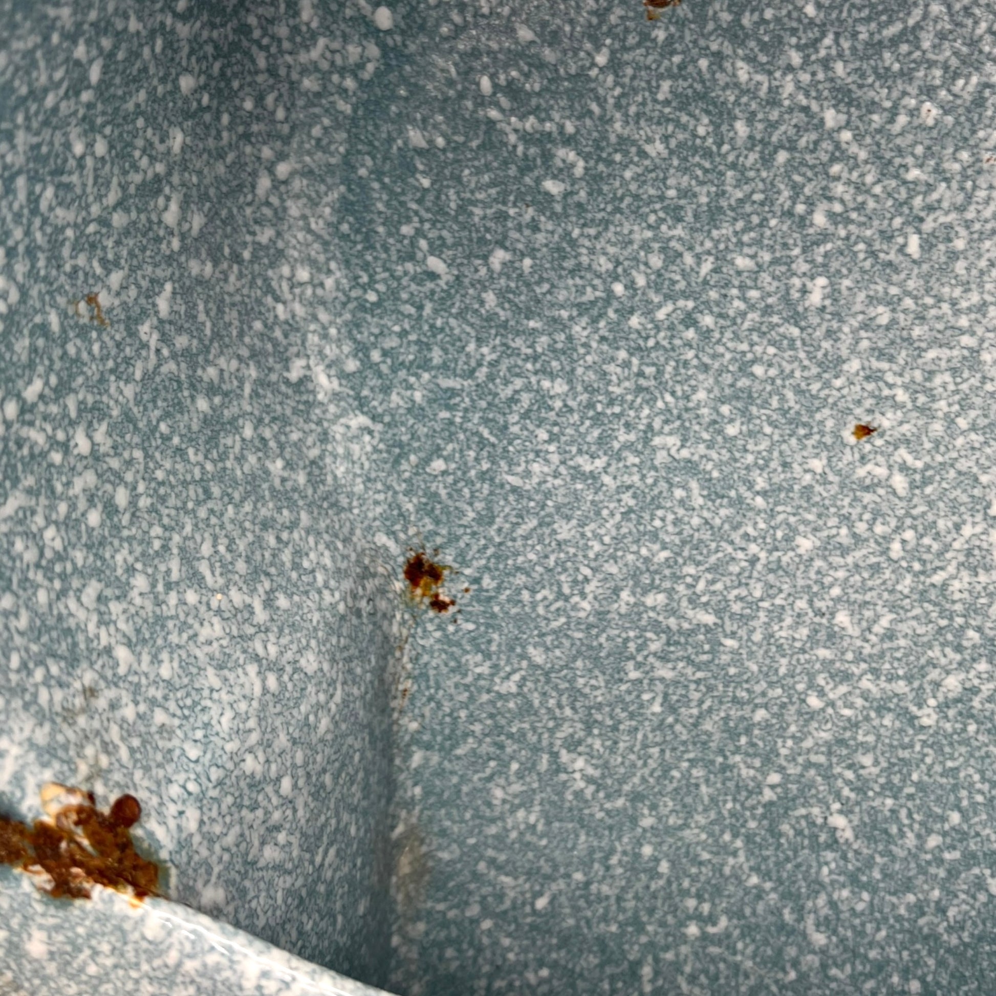 Close-up of wear and tear on a blue metal planter on a white background