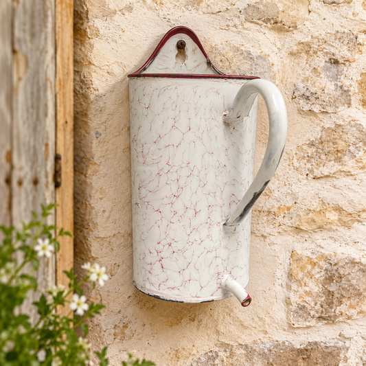 A vintage-style white enamel planter with a red crackle pattern and a dark red rim, mounted on a rustic beige stone wall next to a wooden door.