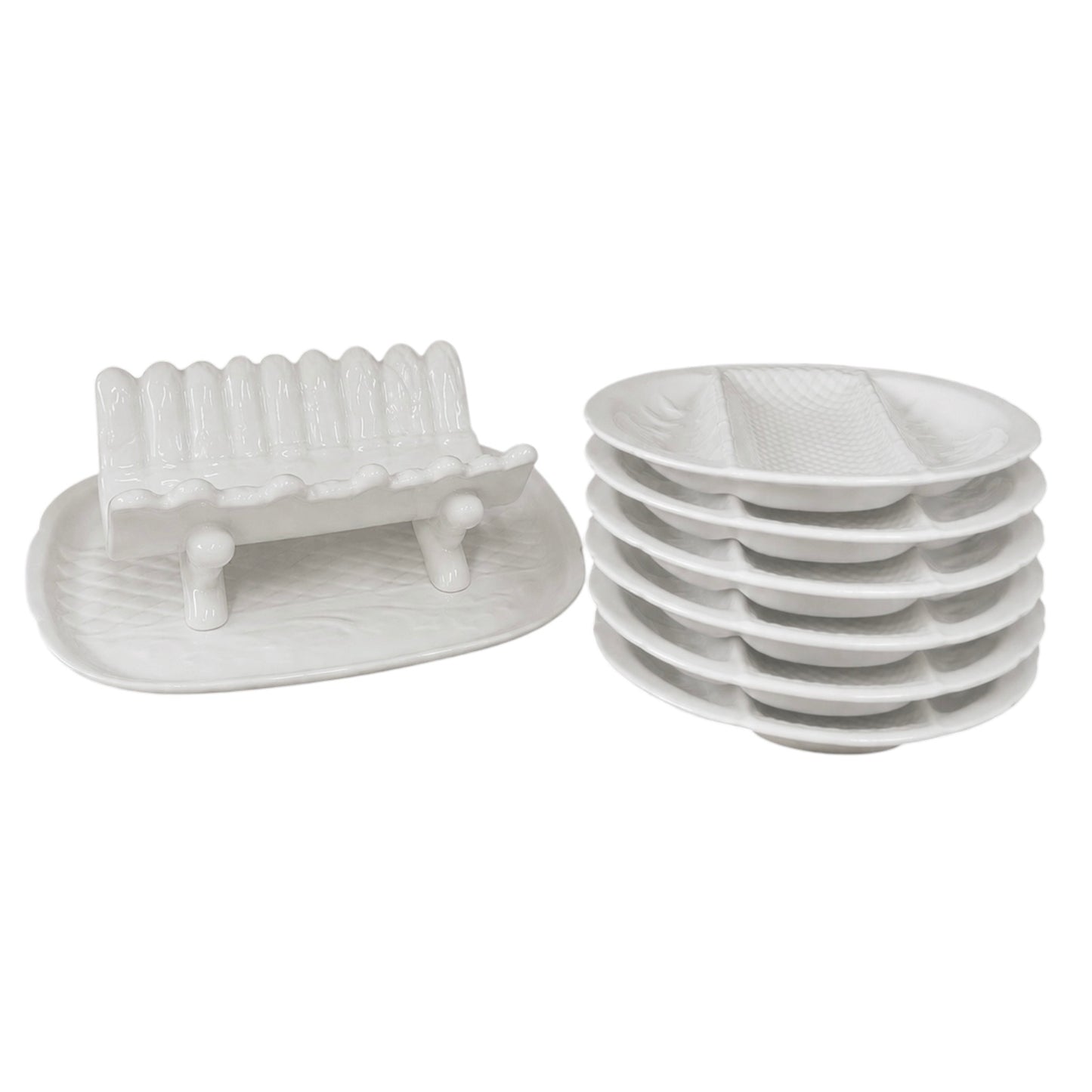 Stacked white ceramic divided serving plates and a matching white ceramic asparagus serving dish displayed on a white background
