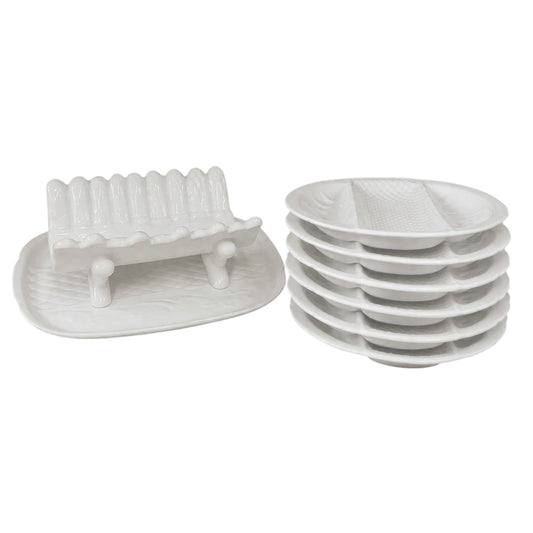 Stacked white ceramic divided serving plates and a matching white ceramic asparagus serving dish displayed on a white background