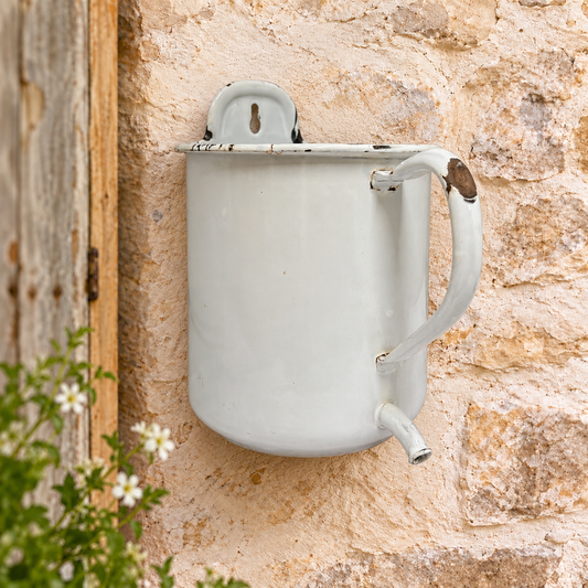 French enamel white irrigator styled as a planter on a garden wall ideal for a rustic garden setting or for use as a herb planter