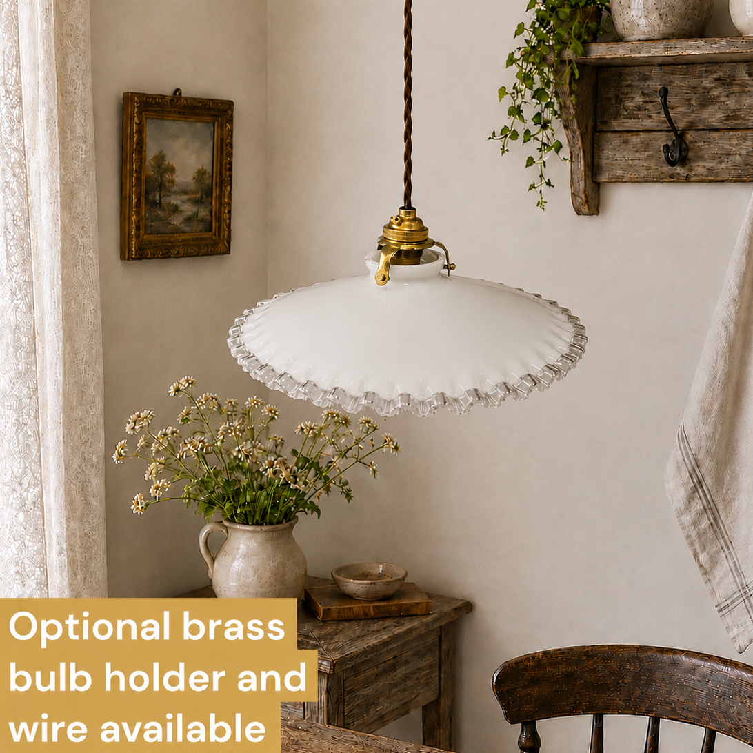 A vintage French milk glass pendant lampshade hangs from the ceiling by a brown twisted wire, adding charm to a rustic home. In the background, a jug of flowers and a chair complete the scene, making it perfect for a period or country-style setting.