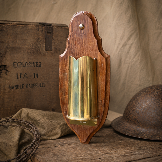 Wooden holder with brass WW1 vase on a rustic surface with military-themed items.
